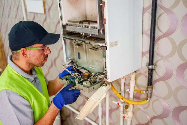 A man in a safety vest and gloves repairs a gas boiler in Frederick, MD
